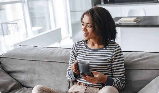 Person relaxing on a sofa with a mug and smartphone, representing easy registration of a SinuSauna device for the extended 90‑day warranty.