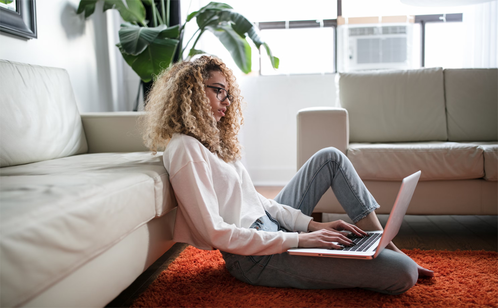 Person sitting on the floor with a laptop in a bright living room, symbolising someone learning about SinuSauna’s respiratory health innovation.