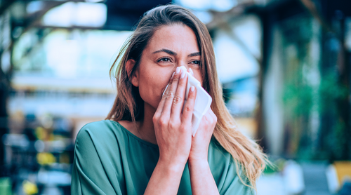 Woman blowing her nose with a tissue in an outdoor setting