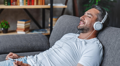 Man wearing headphones and using a smartphone on a couch in a living room.