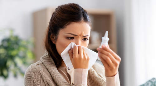 Woman with a cold using a tissue and nasal spray in a home setting
